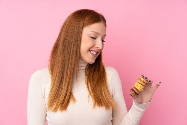 Young redhead woman holding colorful french macarons and happy