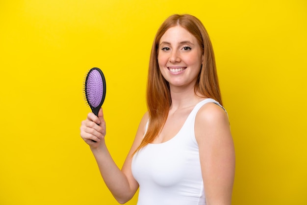 Young redhead woman holding a hairbrush isolated on white background smiling a lot