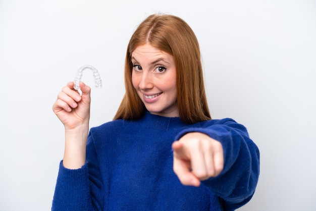 Young redhead woman holding invisible braces isolated on white background points finger at you with a confident expression