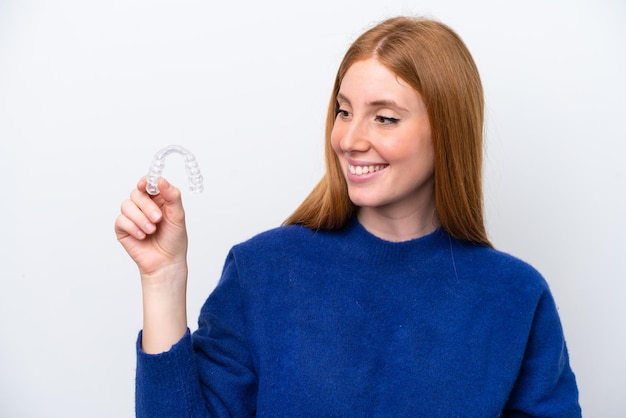 Young redhead woman holding invisible braces isolated on white background with happy expression