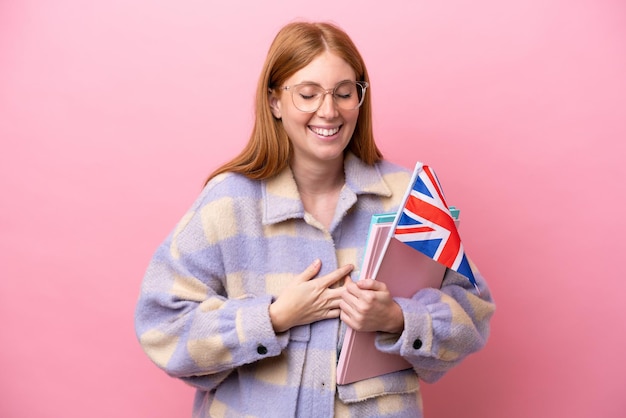 Young redhead woman holding an United Kingdom flag isolated on pink background smiling a lot