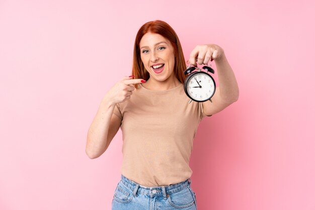 Young redhead woman holding vintage alarm clock