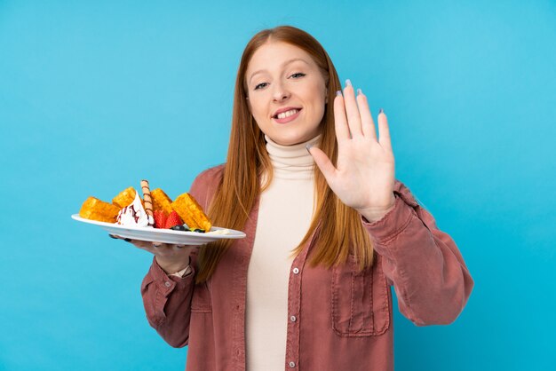 写真 幸せな表情で手で敬礼分離壁にワッフルを置く若い赤毛の女性