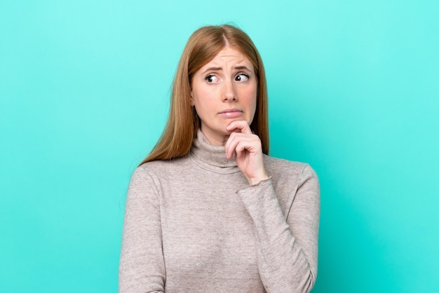 青の背景に疑問を持ち、考えている若い赤毛の女性
