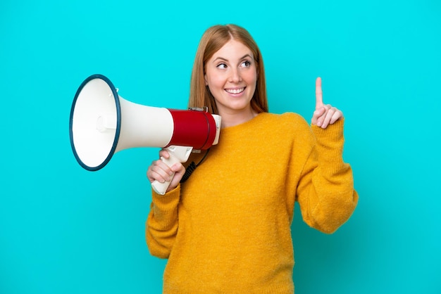 Young redhead woman isolated on blue background holding a megaphone and intending to realizes the solution