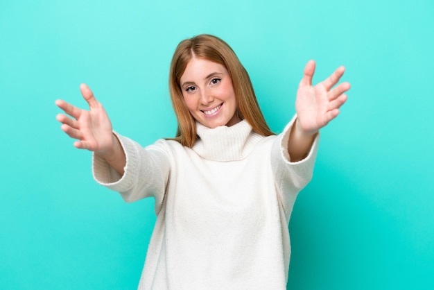 Young redhead woman isolated on blue background presenting and inviting to come with hand