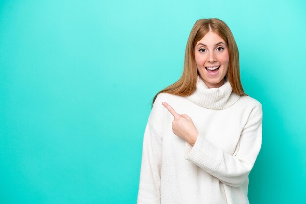 Young redhead woman isolated on blue background surprised and pointing side