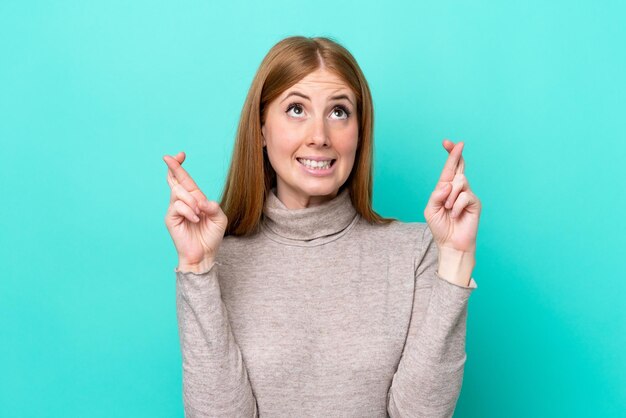 Young redhead woman isolated on blue background with fingers crossing and wishing the best