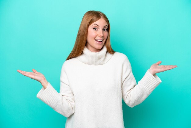 Young redhead woman isolated on blue background with shocked facial expression