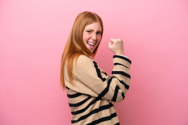 Young redhead woman isolated on pink background celebrating a victory