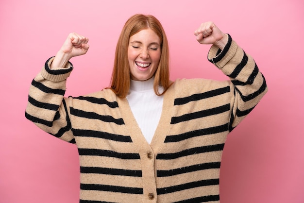 Young redhead woman isolated on pink background doing strong gesture