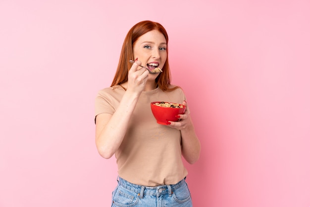 Young redhead woman over isolated pink background holding a bowl of cereals