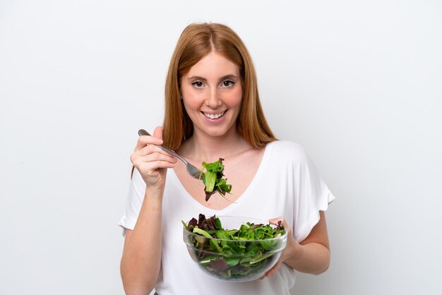 Giovane donna rossa isolata su sfondo bianco in possesso di una ciotola di insalata con felice espressione