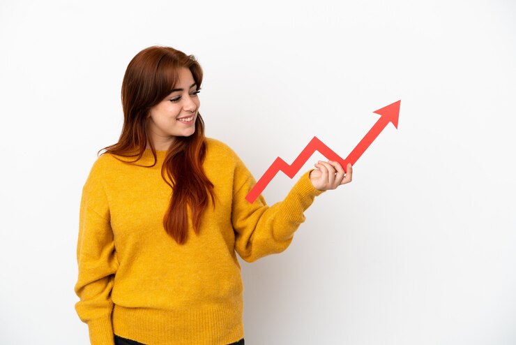 Photo young redhead woman isolated on white background holding a catching a rising arrow with happy expression