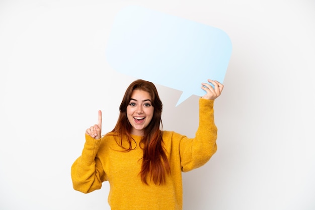 Young redhead woman isolated on white background holding an empty speech bubble with surprised expression