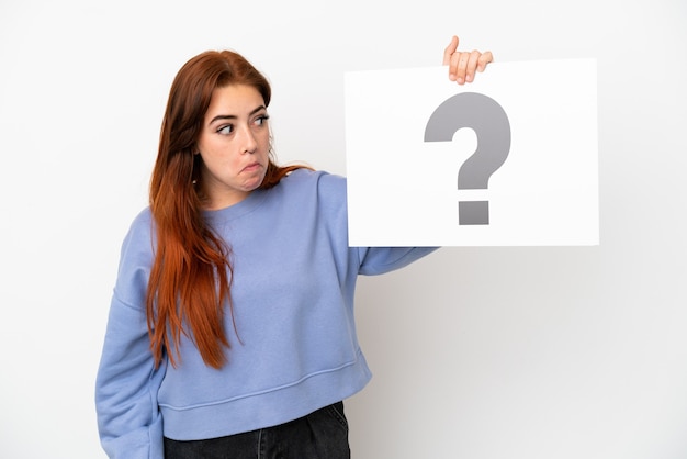 Young redhead woman isolated on white background holding a placard with question mark symbol