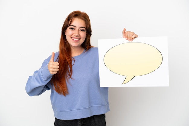 Young redhead woman isolated on white background holding a placard with speech bubble icon with thumb up