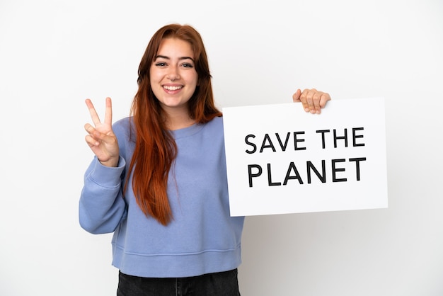 Молодая рыжая женщина, изолированные на белом фоне, держит плакат с текстом «Спасти планету» и празднует победу