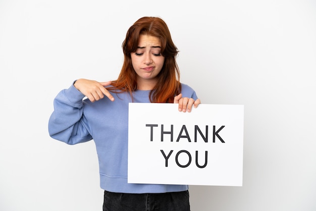 Photo young redhead woman isolated on white background holding a placard with text thank you and  pointing it