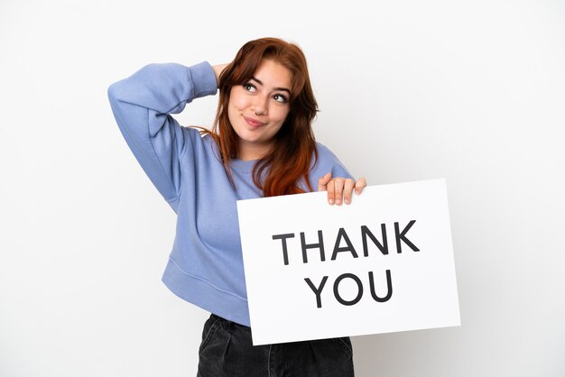 Young redhead woman isolated on white background holding a placard with text THANK YOU and thinking