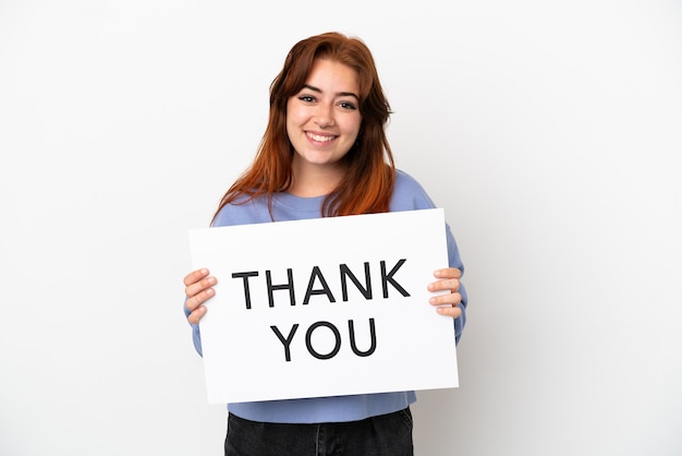 Young redhead woman isolated on white background holding a placard with text THANK YOU with happy expression