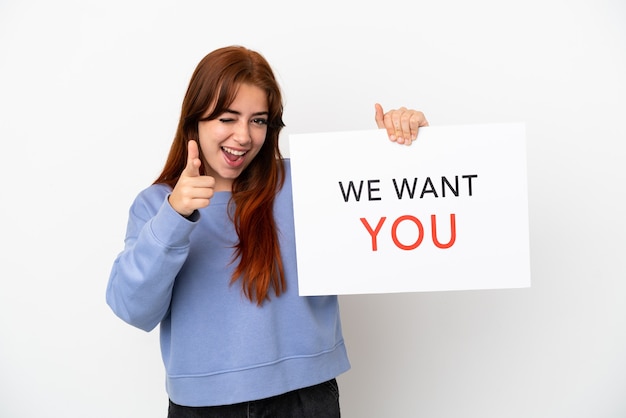 Photo young redhead woman isolated on white background holding we want you board and pointing to the front