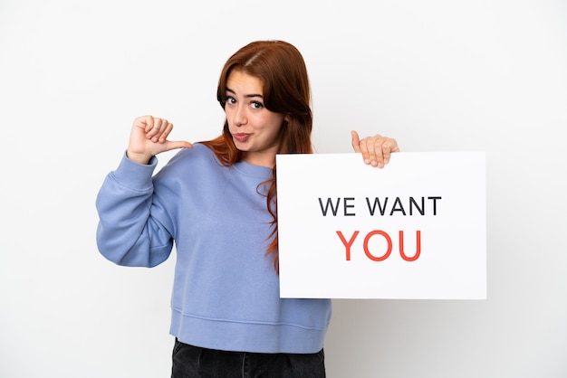 Young redhead woman isolated on white background holding We Want You board with proud gesture