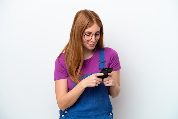 Young redhead woman isolated on white background sending a message with the mobile