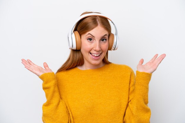 young redhead woman isolated on white background surprised and listening music