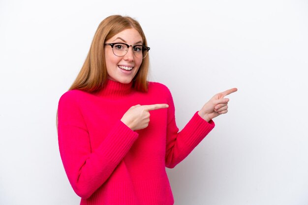 Young redhead woman isolated on white background surprised and pointing side