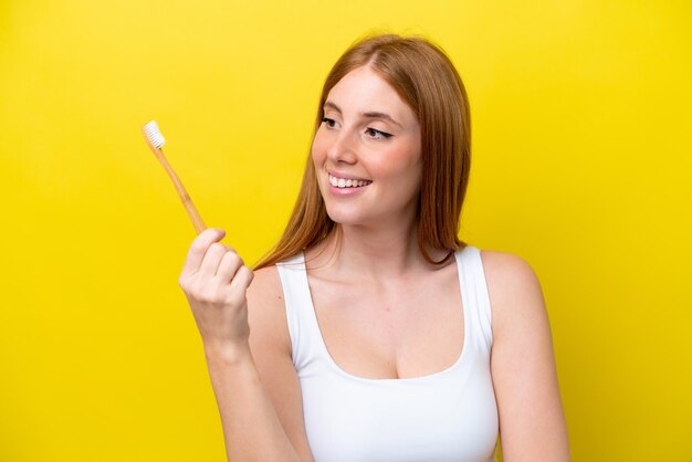 Молодая рыжая женщина изолирована на желтом фоне с зубной щеткой