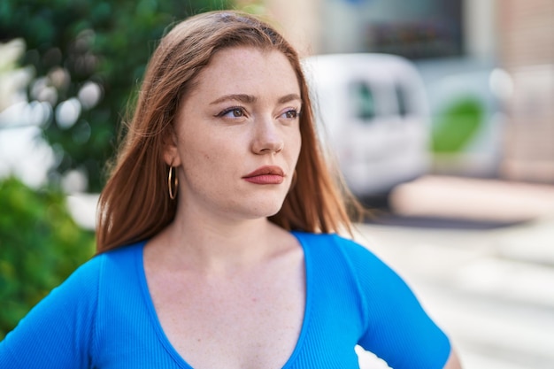 Young redhead woman looking to the side with serious expression at street