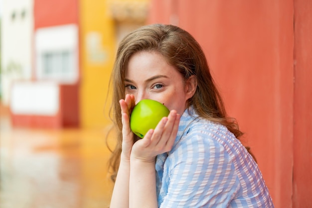 Young redhead woman at outdoors holding an apple