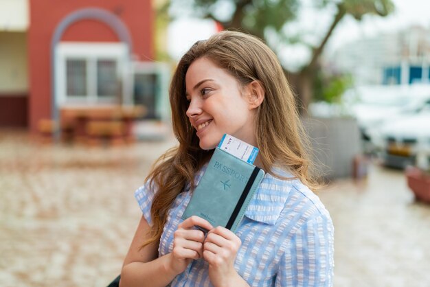 Young redhead woman at outdoors holding a passport with happy expression