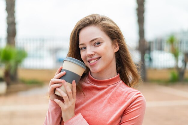 屋外でテイクアウトのコーヒーを持ち、疑問を持っている若い赤毛の女性