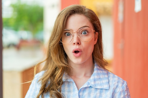 Photo young redhead woman at outdoors with glasses and surprised expression