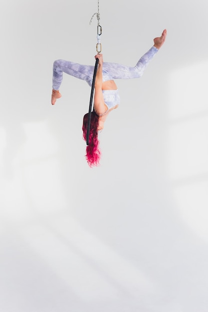 Foto giovane donna dai capelli rossi esegue elementi acrobatici nell'anello d'aria su uno sfondo bianco