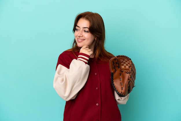 Young redhead woman playing baseball isolated on blue background looking to the side and smiling