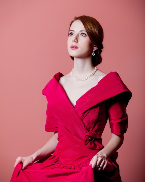 Young redhead woman in red Victorian epoch clothes on pink