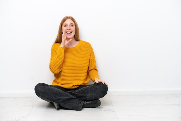 Photo young redhead woman sitting on the floor isolated on white background shouting with mouth wide open