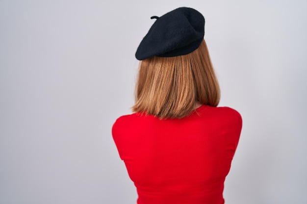 Young redhead woman standing wearing glasses and beret standing backwards looking away with crossed arms