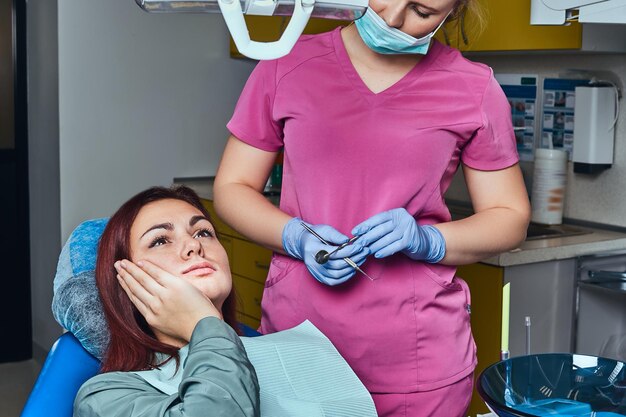 Giovane donna rossa che soffre di mal di denti mentre è seduta su una sedia nell'ufficio del dentista.