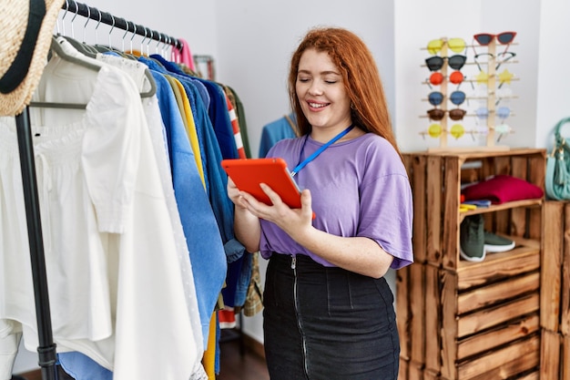 Young redhead woman using touchpad working at clothing store