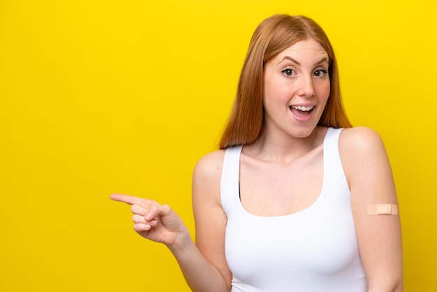 Молодая рыжая женщина в бинтах на желтом фоне удивлена и показывает пальцем в сторону