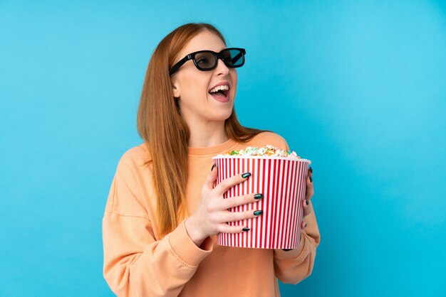 Young redhead woman with 3d glasses and holding a big bucket of popcorns