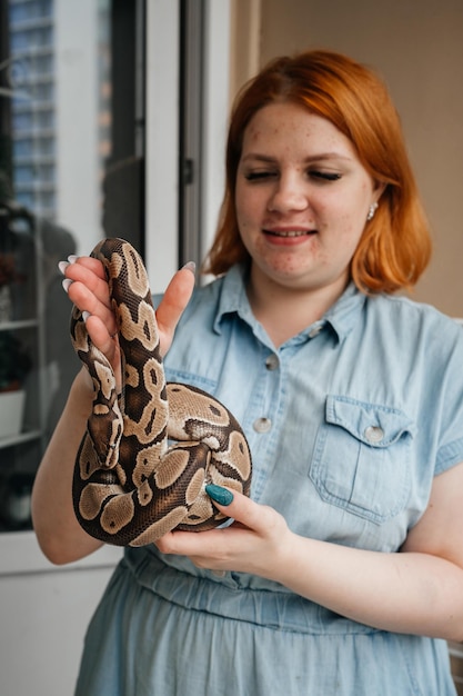 Young redhead woman with acne holdind pet snake in her\
hands