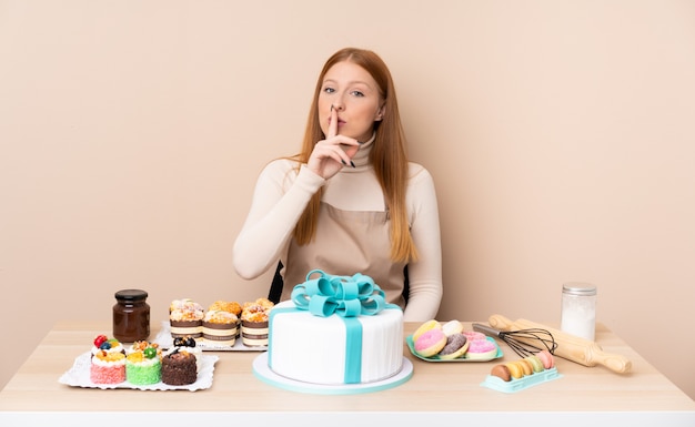沈黙のジェスチャーをしている大きなケーキを持つ若い赤毛の女性