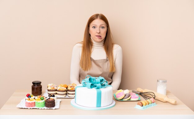 의심과 혼동 얼굴 표정을 가진 큰 케이크와 함께 젊은 빨간 머리 여자