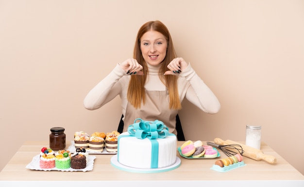 Young redhead woman with a big cake proud and self-satisfied