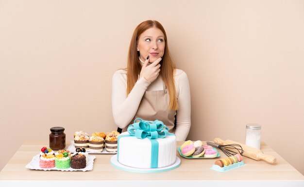 Young redhead woman with a big cake thinking an idea